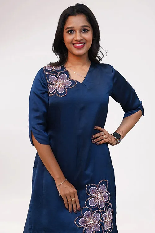 The Almond Blossom Lehenga's navy tunic, a pale lilac blossom worked in beadwork over the left shoulder and more across the hem of the tunic