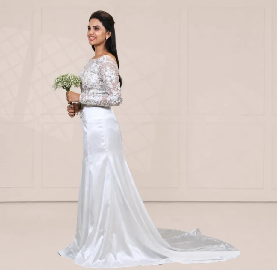 Atelier photograph standing in for the Almond Blossom Gown, Rose: a bride in a white satin gown with a sheer worked bodice, holding a small bouquet against a plain wall