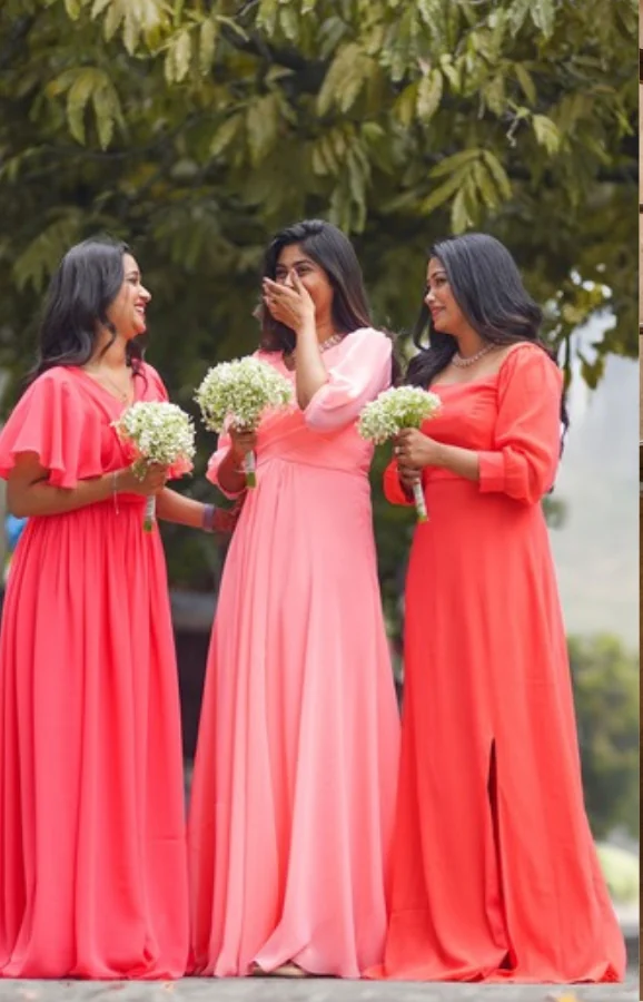 Atelier photograph standing in for the Graceful Gathers: three bridesmaids outdoors under a tree in floor length coral and pink gowns, each holding a small white bouquet